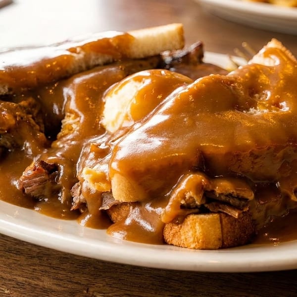 A hearty hot roast beef sandwich with mashed potatoes and gravy on a white plate.