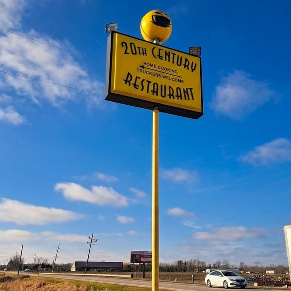 A tall yellow sign for "20th Century Restaurant" with "Home Cooking, Truckers Welcome" against a blue sky.